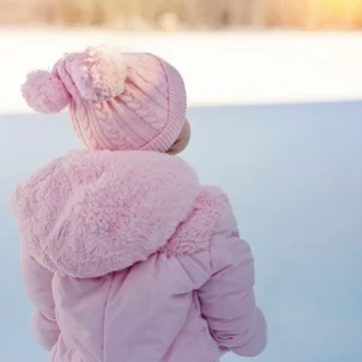 穿粉色外套的孩子背对镜头，站在雪地里